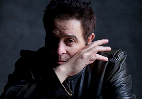 A person in a leather jacket rests their hand near their face, set against a dark background.