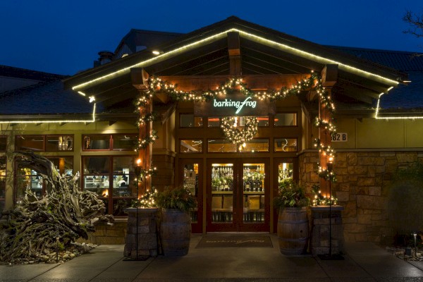 A cozy-looking restaurant exterior at night, with warm lights, wreath, and garland around the entrance, inviting guests in.