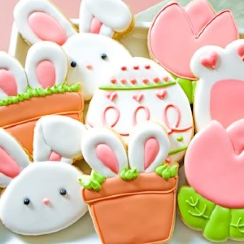 A plate of colorful cookies featuring bunnies, eggs, flowers, and carrots, all decorated with pastel icing.
