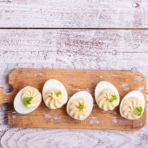 Deviled eggs on a wooden board, garnished with herbs, placed on a rustic white surface.