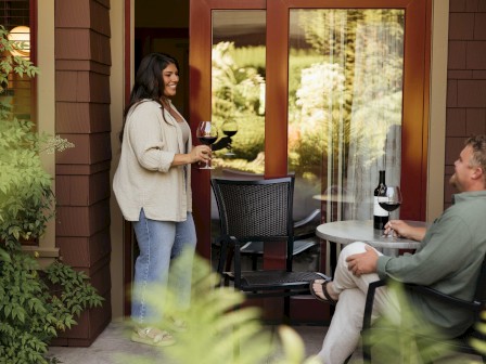 A woman and man enjoying wine on a patio with a table and plants around them.