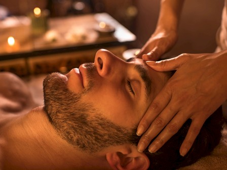 A person receives a facial massage in a serene setting, with soft lighting and candles, creating a relaxing ambiance.
