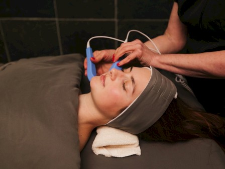 A person is receiving a facial treatment with a handheld device, while lying down with a towel under their head.