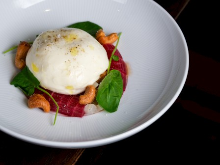 Poached egg with beets, greens, cashews and onion in a white bowl.