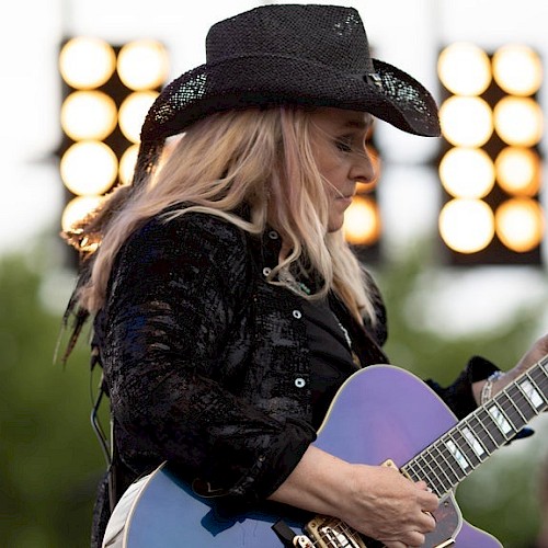 A woman wearing a black cowboy hat and playing a guitar