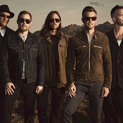 Five men standing in a desert area, posing for the camera