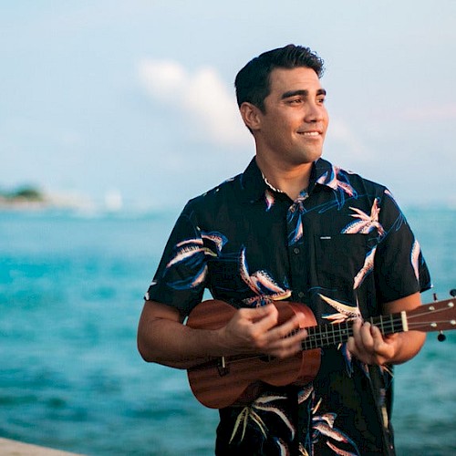 Man standing on a beach playing the ukulele