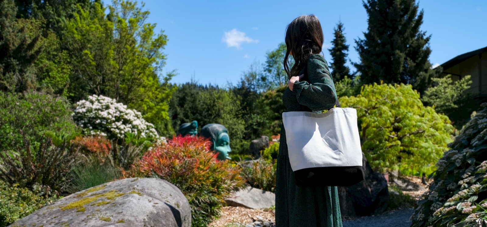 A woman with a tote bag standing outside in a garden area