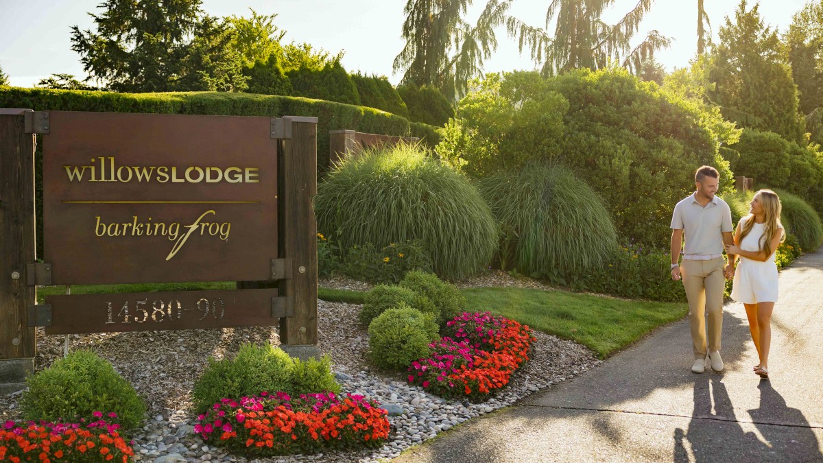 A couple walks happily along a garden path near the Willow Lodge with colorful flowers and lush greenery.