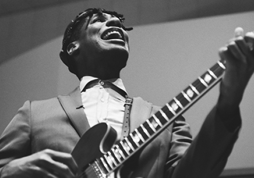 A musician passionately playing an electric guitar while singing, captured in black and white.