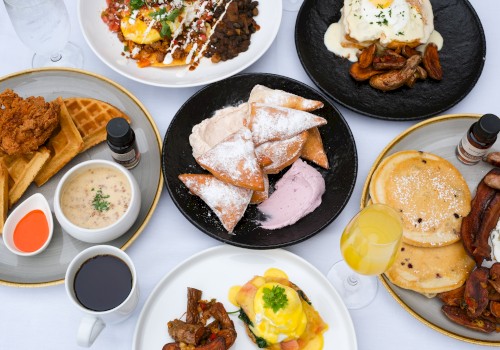 A spread of breakfast foods including waffles, tacos, pastries, pancakes, a savory dish, and beverages is shown on a white table.