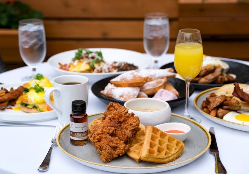 A table set with brunch items: fried chicken, waffles, beignets, eggs, bacon, coffee, orange juice, and a small syrup bottle.