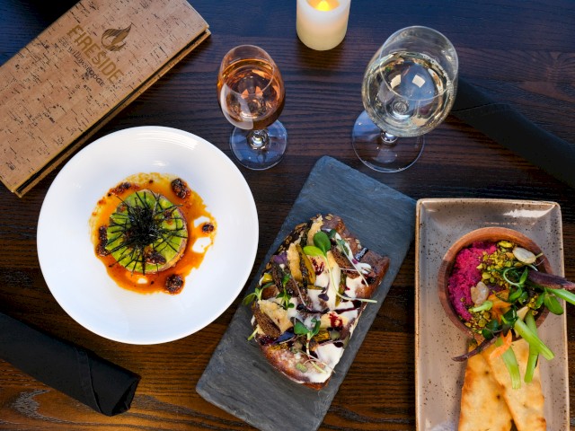 This image shows a fancy dinner setup with dishes, wine glasses, a candle, and a menu on a dark wooden table.