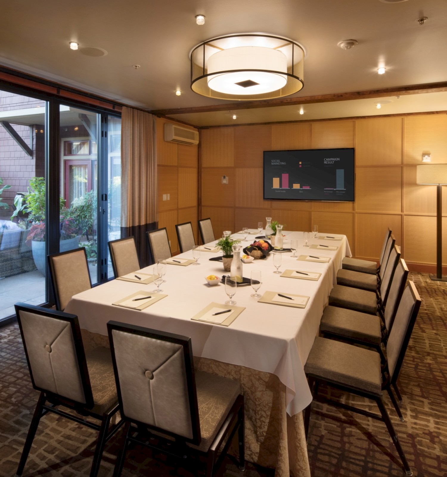 A conference room with a long table, set for a meeting or meal, adorned with flowers and a chart on the wall.