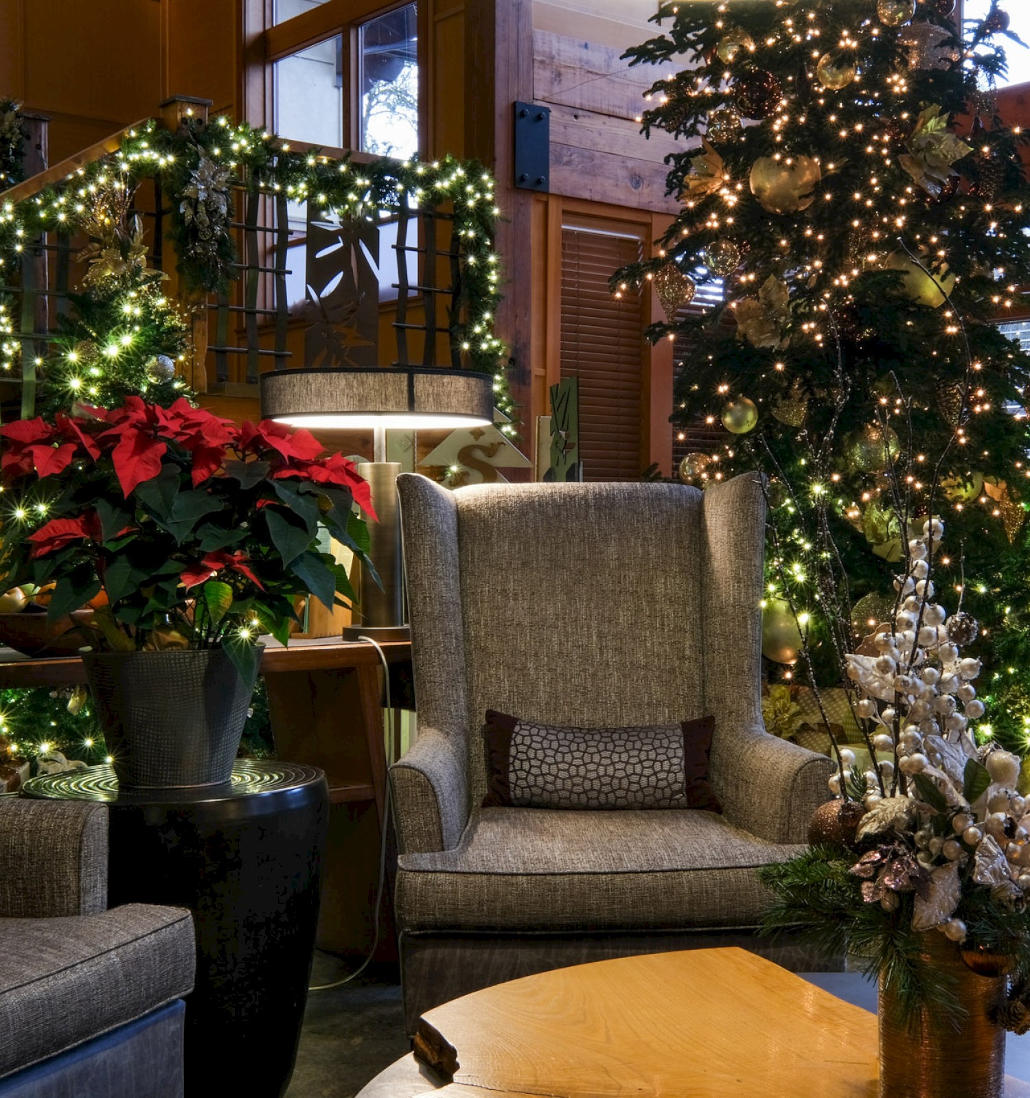 A cozy, decorated living room with Christmas trees, wreaths, poinsettias, and festive lighting creating a warm holiday atmosphere.