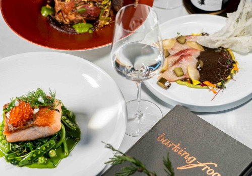 The image shows an elegant dining setup with gourmet dishes, wine, and a menu from 