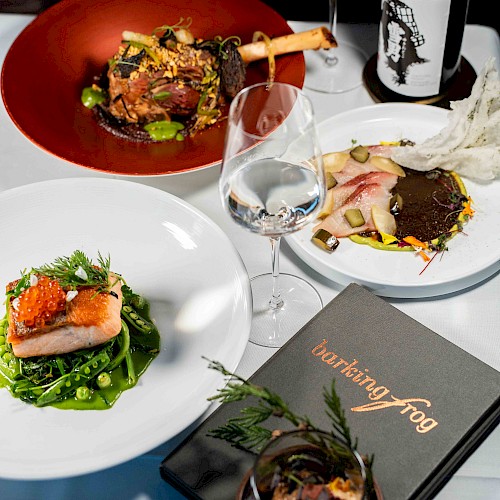 The image shows an elegant dining setup with gourmet dishes, wine, and a menu from 